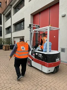 Operatrice su carrello elevatore durante una lezione pratica, accompagnata dall'istruttore in un'area esterna.